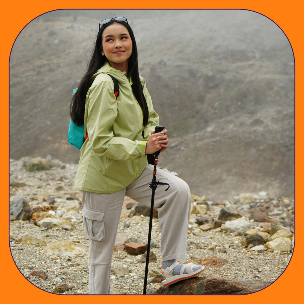 Woman hiking in rugged mountains wearing outdoor gear and holding trekking poles.